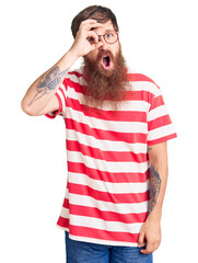 Wall Mural - Handsome young red head man with long beard wearing casual clothes doing ok gesture shocked with surprised face, eye looking through fingers. unbelieving expression.