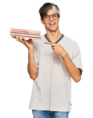 Canvas Print - Young hispanic man holding books smiling happy pointing with hand and finger