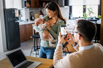 Wall Mural - Proud father take picture of his wife with infant baby at home. Happy family, technology concept.