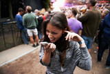 Fototapeta  - Music festival, event and woman outdoor with phone call, conversation and noise from concert, crowd or party. Contact, person and confused by loud, sound or listening to smartphone and lost at a rave