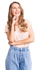 Poster - Young beautiful caucasian woman with blond hair wearing casual clothes with hand on chin thinking about question, pensive expression. smiling and thoughtful face. doubt concept.