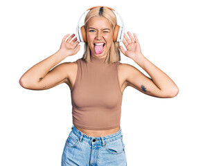 Canvas Print - Beautiful young blonde woman listening to music using headphones sticking tongue out happy with funny expression.