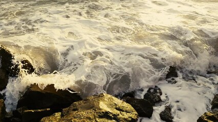 Wall Mural - Surf on the stones of the Mediterranean coast. Waves run over dark stones. Amazing shapes of the rocky shore. Slow motion