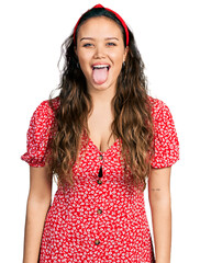 Wall Mural - Young hispanic girl wearing casual clothes sticking tongue out happy with funny expression. emotion concept.