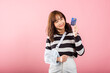 © sorapop - An Asian woman smiles confidently despite her broken arm. She relies on a credit card to cover medical expenses after an accident. Happy female with a sling-supported hand, isolated on pink background