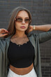 © alones - Urban stylish female portrait of a beautiful fashion woman with vintage sunglasses in fashionable clothes with a shirt standing near a black brick wall. Pretty cool girl