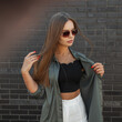 © alones - Street beautiful elegant model girl with vintage sunglasses in a fashion shirt with a top stands near a black brick wall