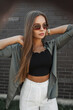 © alones - Fashionable beautiful young business woman with vintage sunglasses in fashion clothes stands near a black brick wall. Trendy chic lady