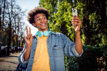 Canvas Print - Photo of cool good mood guy dressed jeans shirt headphones showing v-sign recording video vlog modern gadget outdoors urban city park