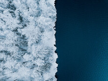 Aerial View Of Blue Water Sea And Snow Covered Trees Woods In Winter Finland.