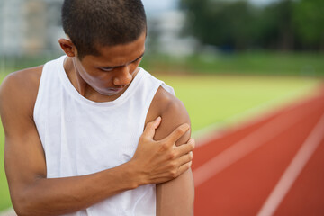 Athletes sport man runner wearing white sportswear to sitting feeling pain in his shoulder after practicing on a running track at a stadium, copy space. Runner sport injury concept.