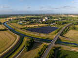 Fototapeta Niebo - Drone Shot of solar panels at a sunny day between fields, river and a street.