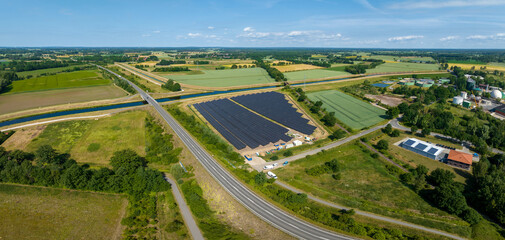 Wall Mural - Panorama of solar panels at a sunny day between fields, river and a street.