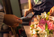 Close up of female hands using credit card for paying using payment terminal in flower shop.