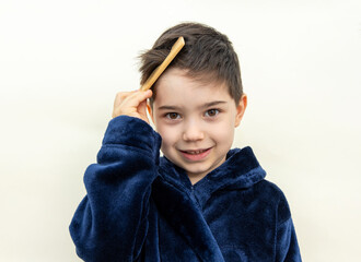 cute adorable preschooler kid boy brushing hair in front of double sided mirror or isolated on beige.child using eco wooden comb, dressed in bathrobe.space for text advertising banner