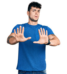 Sticker - Young hispanic man wearing casual t shirt doing stop gesture with hands palms, angry and frustration expression