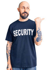 Wall Mural - Young handsome man wearing security t shirt smiling with happy face looking and pointing to the side with thumb up.