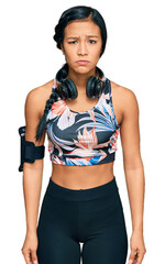 Wall Mural - Beautiful hispanic woman wearing sportswear and headphones skeptic and nervous, frowning upset because of problem. negative person.