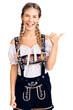 © Krakenimages.com - Beautiful caucasian woman with blonde hair wearing octoberfest traditional clothes smiling with happy face looking and pointing to the side with thumb up.