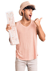 Canvas Print - Young hispanic man wearing summer hat holding map pointing thumb up to the side smiling happy with open mouth