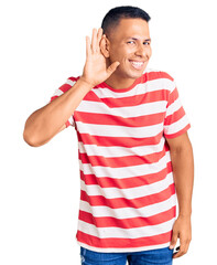 Wall Mural - Young handsome latin man wearing casual clothes smiling with hand over ear listening an hearing to rumor or gossip. deafness concept.