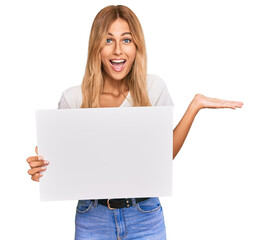 Sticker - Beautiful blonde young woman holding blank empty banner celebrating victory with happy smile and winner expression with raised hands