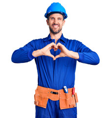 Canvas Print - Young handsome man wearing worker uniform and hardhat smiling in love doing heart symbol shape with hands. romantic concept.