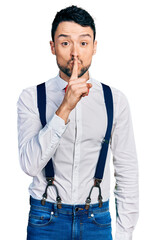 Poster - Hispanic man with beard wearing hipster look with bow tie and suspenders asking to be quiet with finger on lips. silence and secret concept.