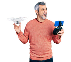 Poster - Middle age hispanic man with grey hair using drone with remote control angry and mad screaming frustrated and furious, shouting with anger. rage and aggressive concept.