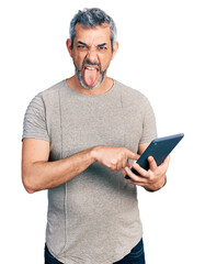 Sticker - Middle age hispanic with grey hair using touchpad device sticking tongue out happy with funny expression.