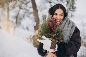 Wall Mural - Happy pretty smiling woman holding bouquet of pine tree in snowy forest in winter.