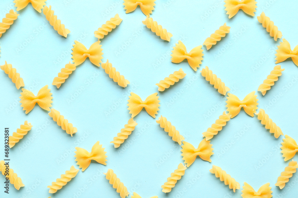 Composition with uncooked farfalle and fusilli pasta on blue background