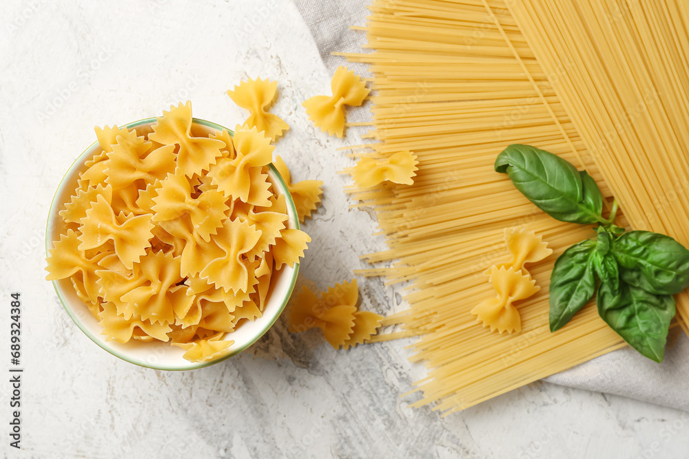Bowl with uncooked farfalle and spaghetti pasta on light background