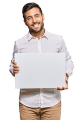 Wall Mural - Handsome hispanic man holding blank empty banner looking positive and happy standing and smiling with a confident smile showing teeth