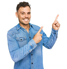 Sticker - Young hispanic man wearing casual denim jacket smiling and looking at the camera pointing with two hands and fingers to the side.