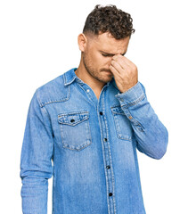 Poster - Young hispanic man wearing casual denim jacket tired rubbing nose and eyes feeling fatigue and headache. stress and frustration concept.