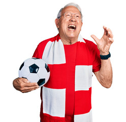 Wall Mural - Senior man with grey hair football hooligan holding ball crazy and mad shouting and yelling with aggressive expression and arms raised. frustration concept.