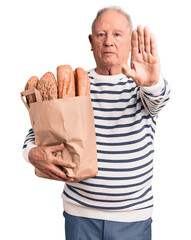 Canvas Print - Senior handsome grey-haired man holding paper bag with bread with open hand doing stop sign with serious and confident expression, defense gesture