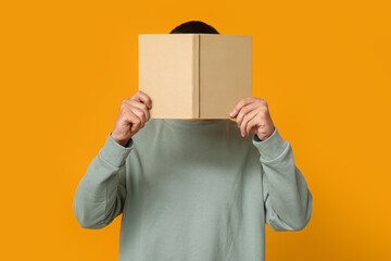 Young man covering face while reading book on orange background