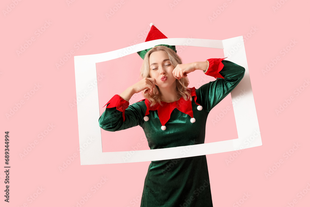 Funny young woman dressed as elf with frame on pink background