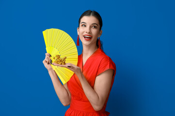 Poster - Beautiful young shocked woman with golden dragon figurine and fan on blue background. Chinese New Year celebration