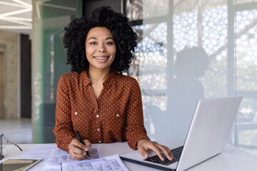 Happy african american businesswoman working in office sitting at desk in front of laptop smiling and looking at camera.