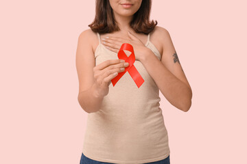 Wall Mural - Pretty young woman with red ribbon on pink background. World AIDS Day