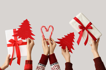 Wall Mural - Hands holding Christmas gifts, candy canes and paper fir trees on grey background