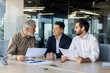 © Liubomir - Group of businessmen sitting in the office at the table, holding work documents, holding a work meeting, discussing important issues.
