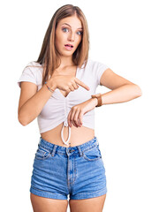 Wall Mural - Young beautiful blonde woman wearing casual white tshirt in hurry pointing to watch time, impatience, upset and angry for deadline delay