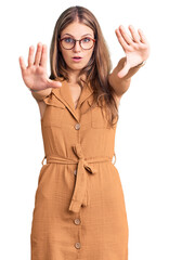 Wall Mural - Young beautiful blonde woman wearing casual clothes and glasses doing stop gesture with hands palms, angry and frustration expression