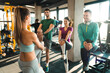 Group of smiling athletic people following warming up instructions of their beautiful female fitness coach before gym workout. Female fitness instructor stretching with a group of three people in gym.