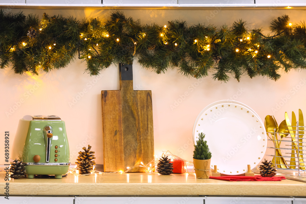 Utensils on counter with Christmas lights and fir branches in kitchen