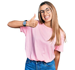 Wall Mural - Hispanic young woman wearing casual t shirt and glasses smiling happy and positive, thumb up doing excellent and approval sign